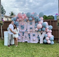 a couple standing in front of a balloon arch with the word oh baby