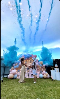 a couple standing in front of a blue and white balloon arch